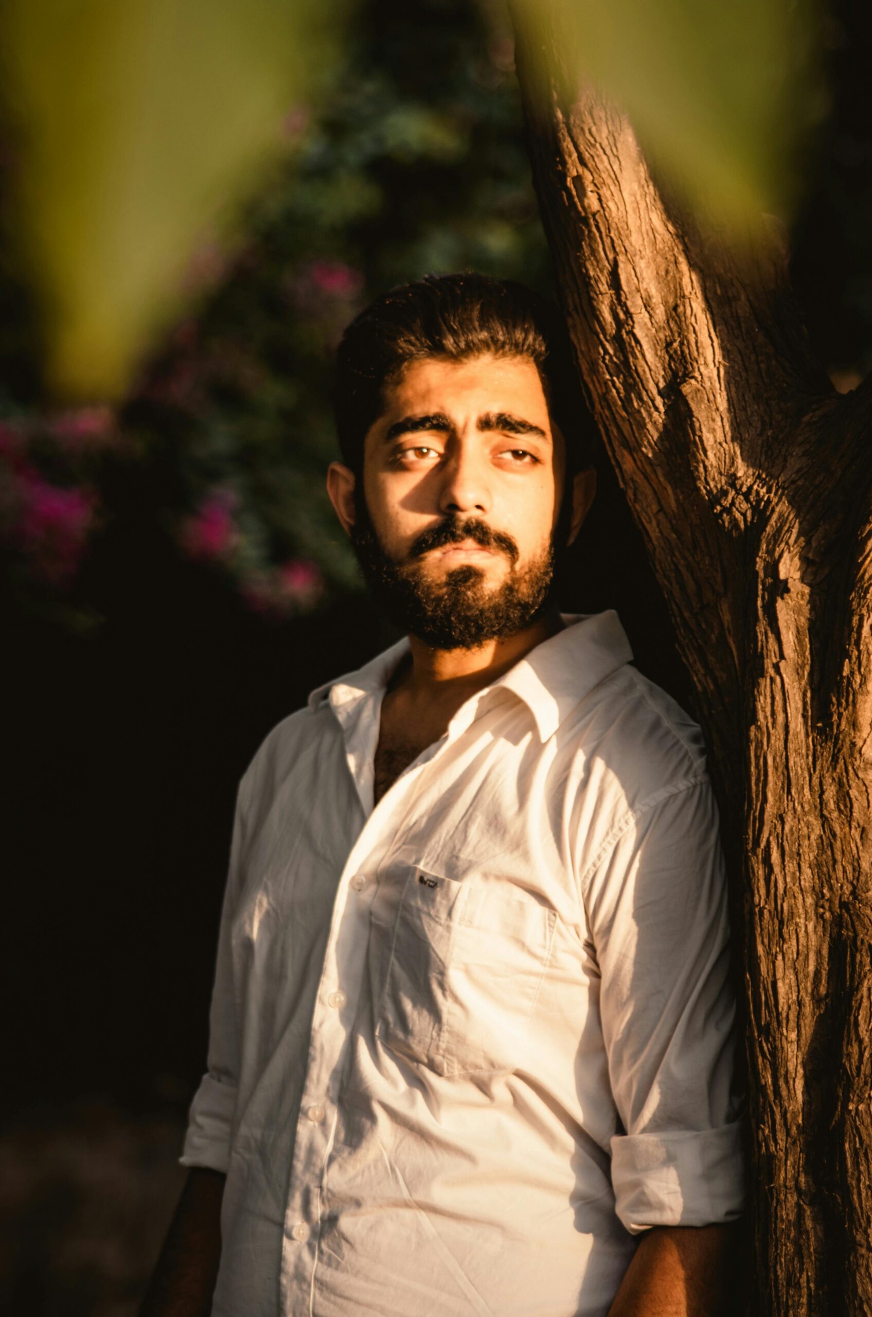 Reviews / Testimonials Page Thoughtful man with beard and white shirt leans on a tree in warm sunlight.